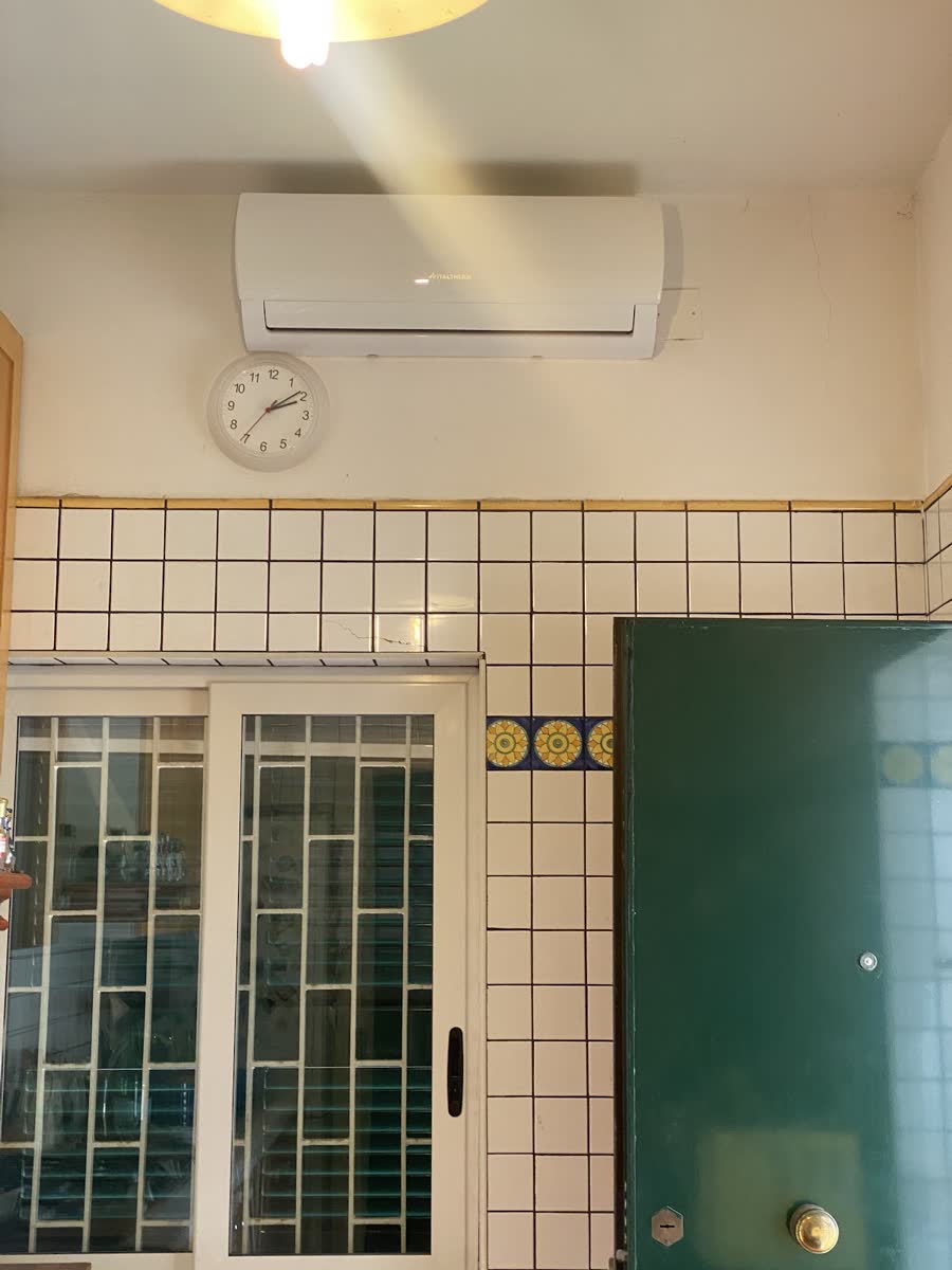 Climatizzatore a parete installato sopra la porta finestra di una cucina con piastrelle bianche